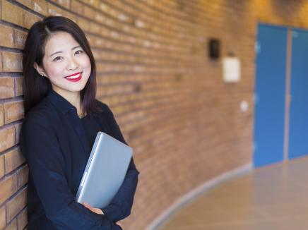 South Korean college student stands in a hallway with her laptop. 