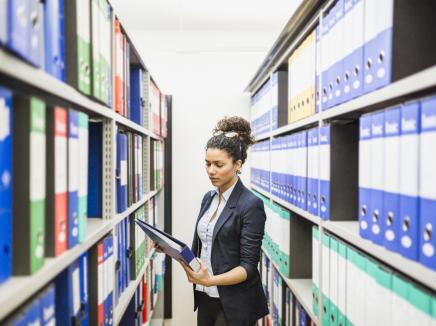 Young woman looks at binder while standing between two shelves