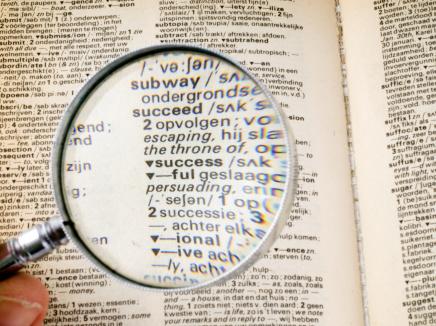 Person examines dictionary with looking glass. 