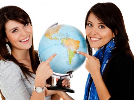 Female students pose next to globe. 