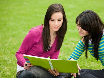 Young women look at a book while sitting on the grass. 