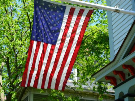 American flag hanging from a flagpole on a house with trees. 